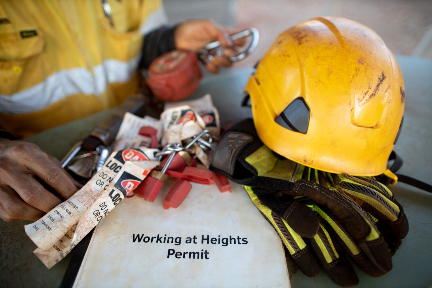 Safety workplace working at height permit book helmet personal locks place on the table with defocused inspector inspecting an inertia reel shock absorbing fall protection device prior used background